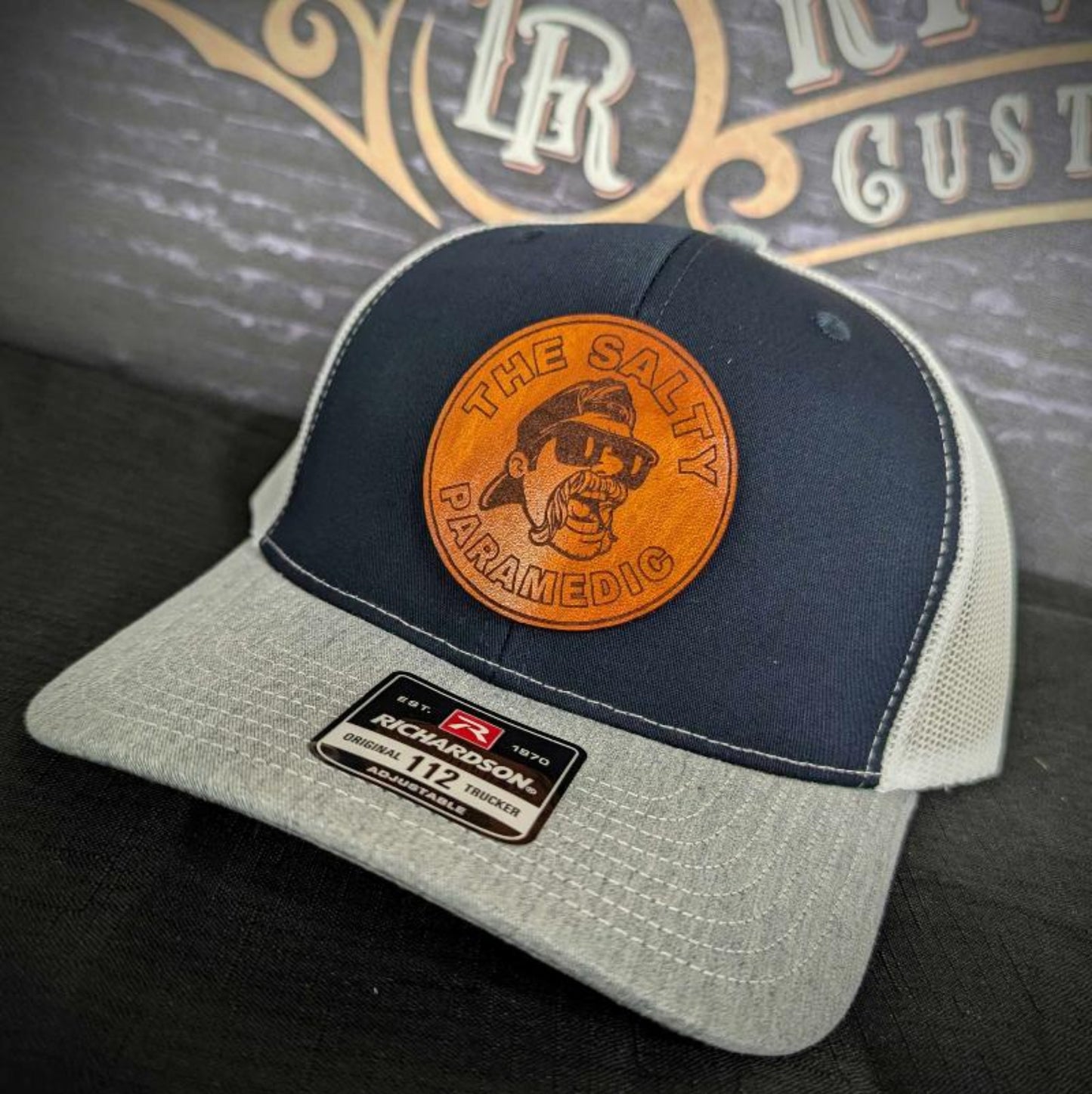Custom firefighter and EMS hats featuring The Salty Paramedic's leather patch design, shown on Richardson 112 and 110 hats for first responders.