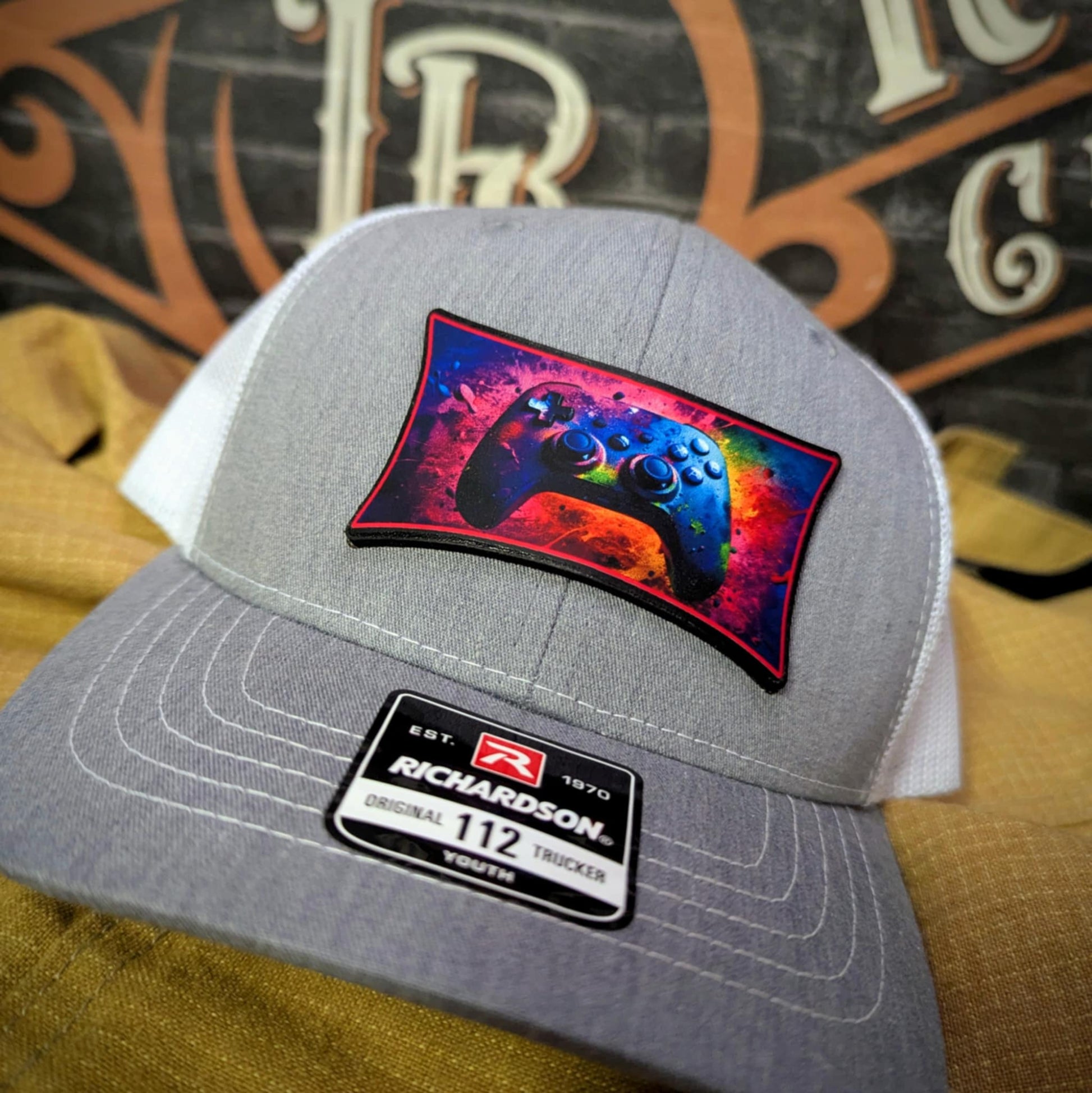 Custom hat with full-color leather patch of neon video game controller on gray and white trucker cap