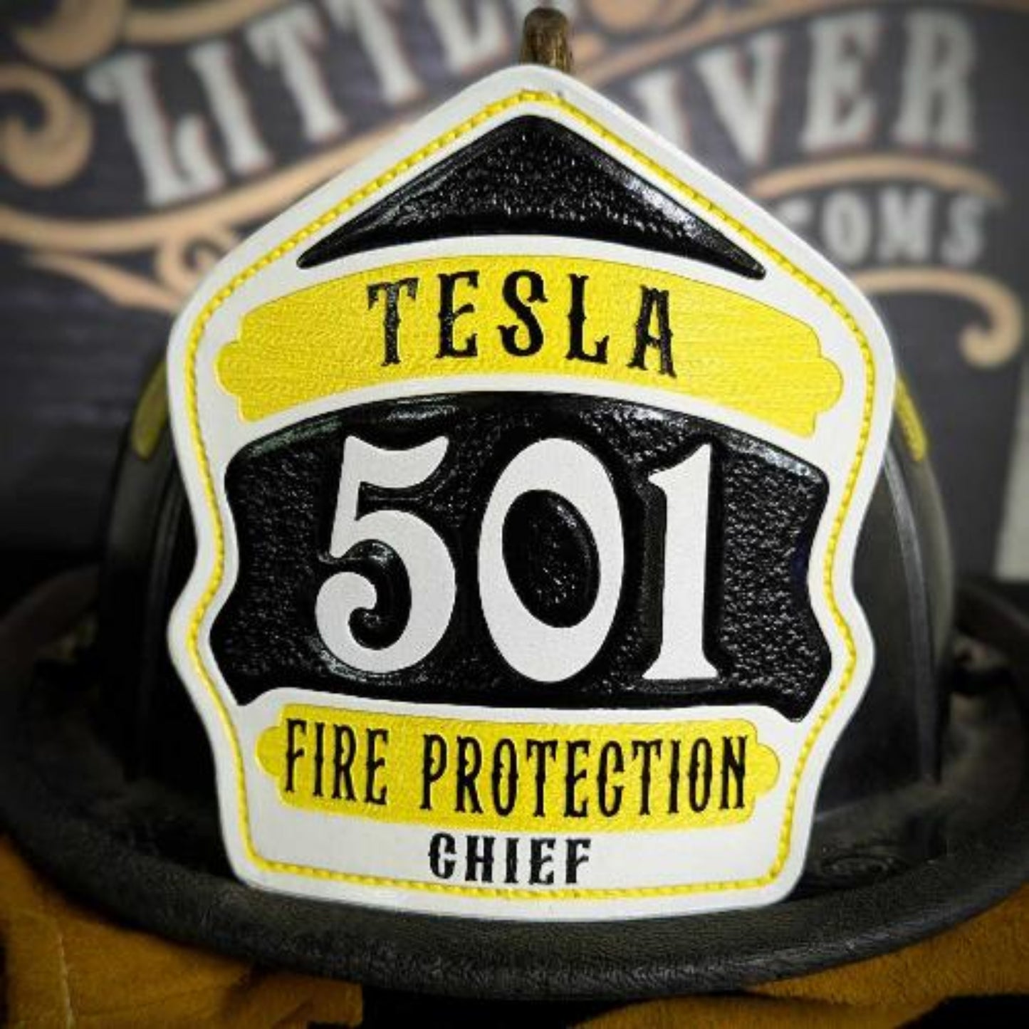White and yellow chief-style leather firefighter helmet shield with large numerals on a black center panel, hand-painted and mounted on a helmet.