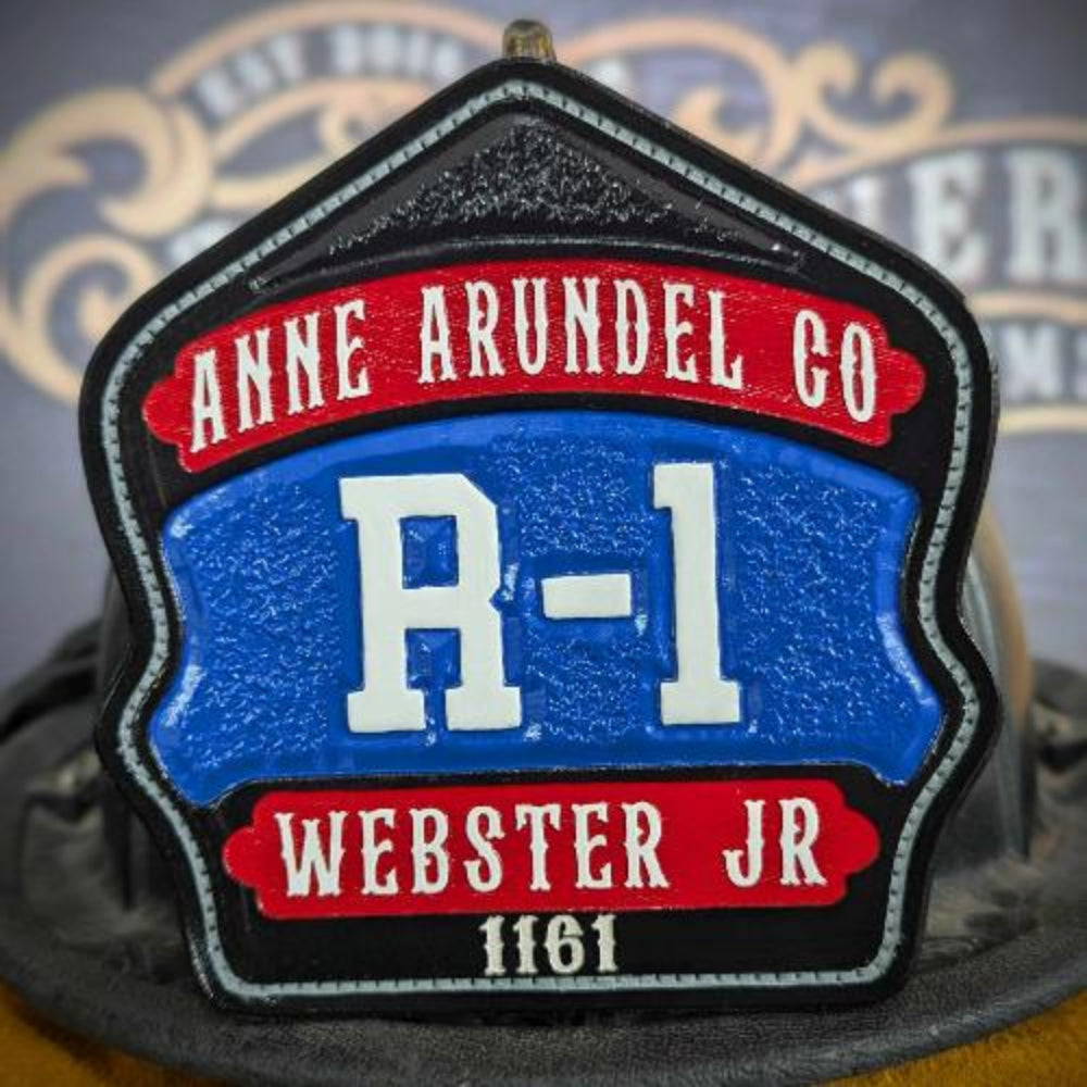 Custom leather firefighter helmet shield with blue center panel and red top/bottom banners—white block insignia on a textured black background, mounted on a helmet.