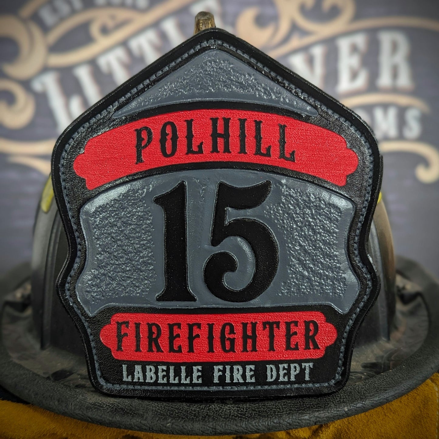 ustom leather firefighter helmet shield with gray center panel, red top and bottom banners, and bold black numeral—hand-painted and mounted on a helmet.