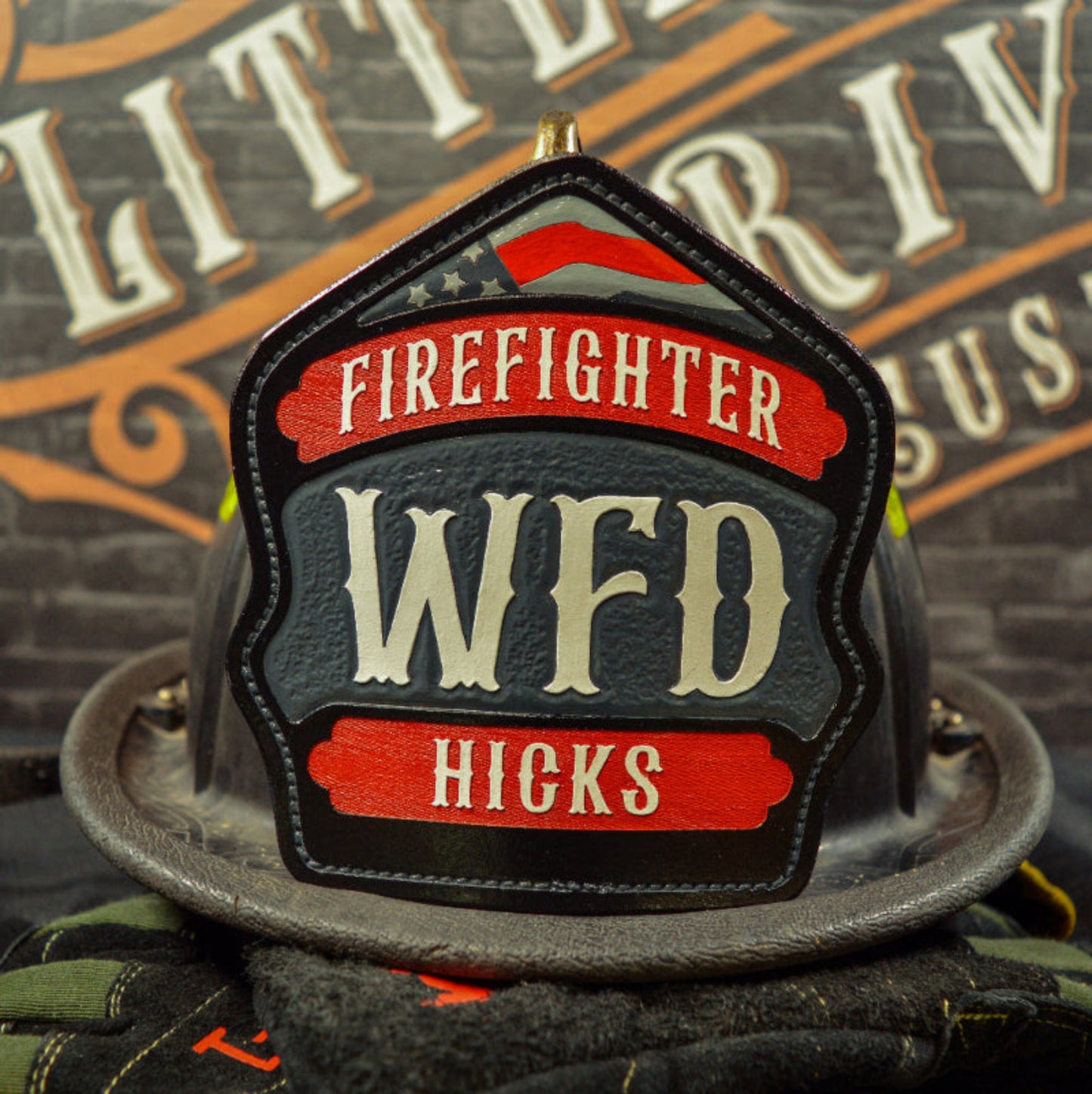 Custom leather firefighter helmet shield with red top and bottom banners, gray center panel, and subtle flag detail—hand-painted and mounted on a helmet.