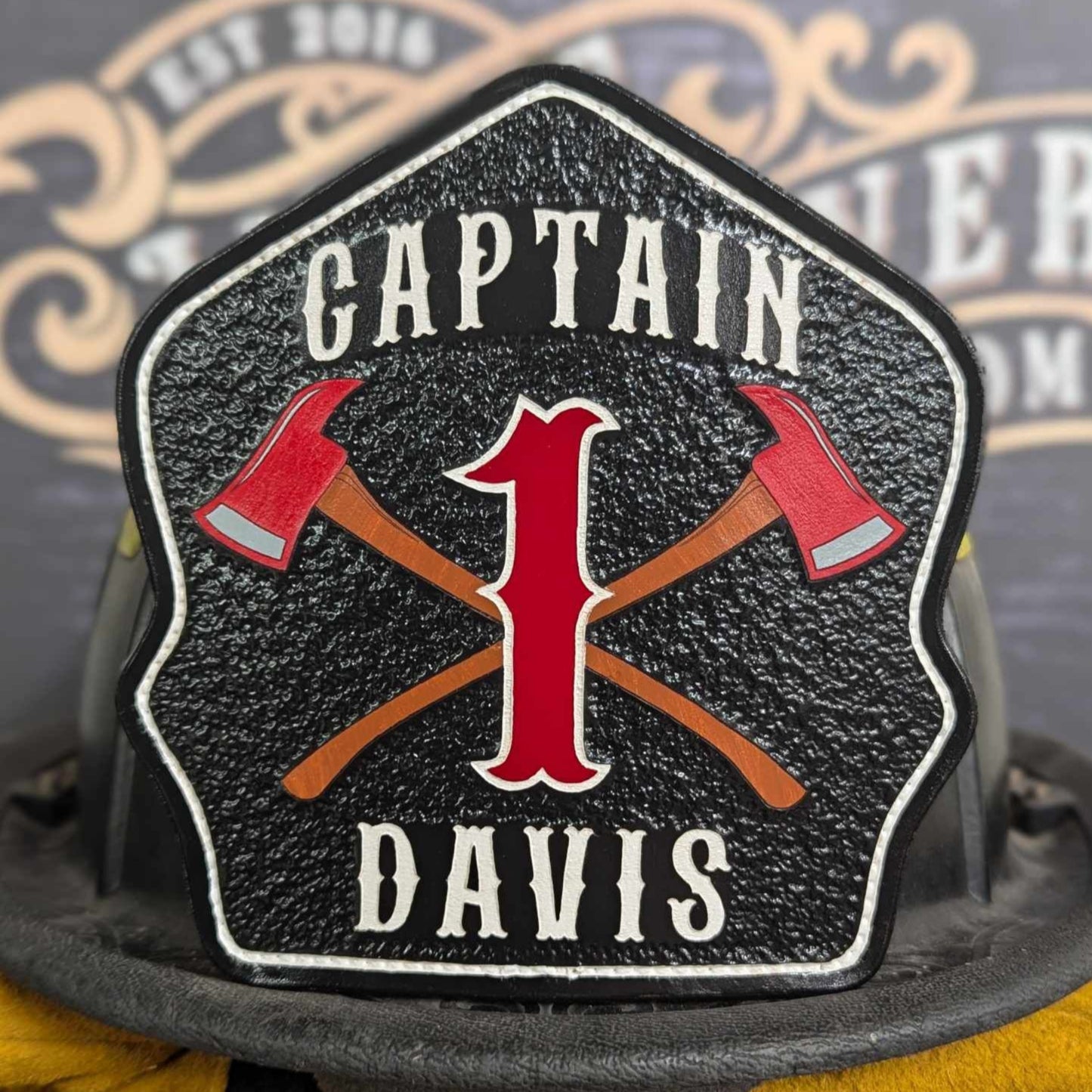 Black leather firefighter helmet shield with crossed red axes and bold red number 1, custom fire department gear.
