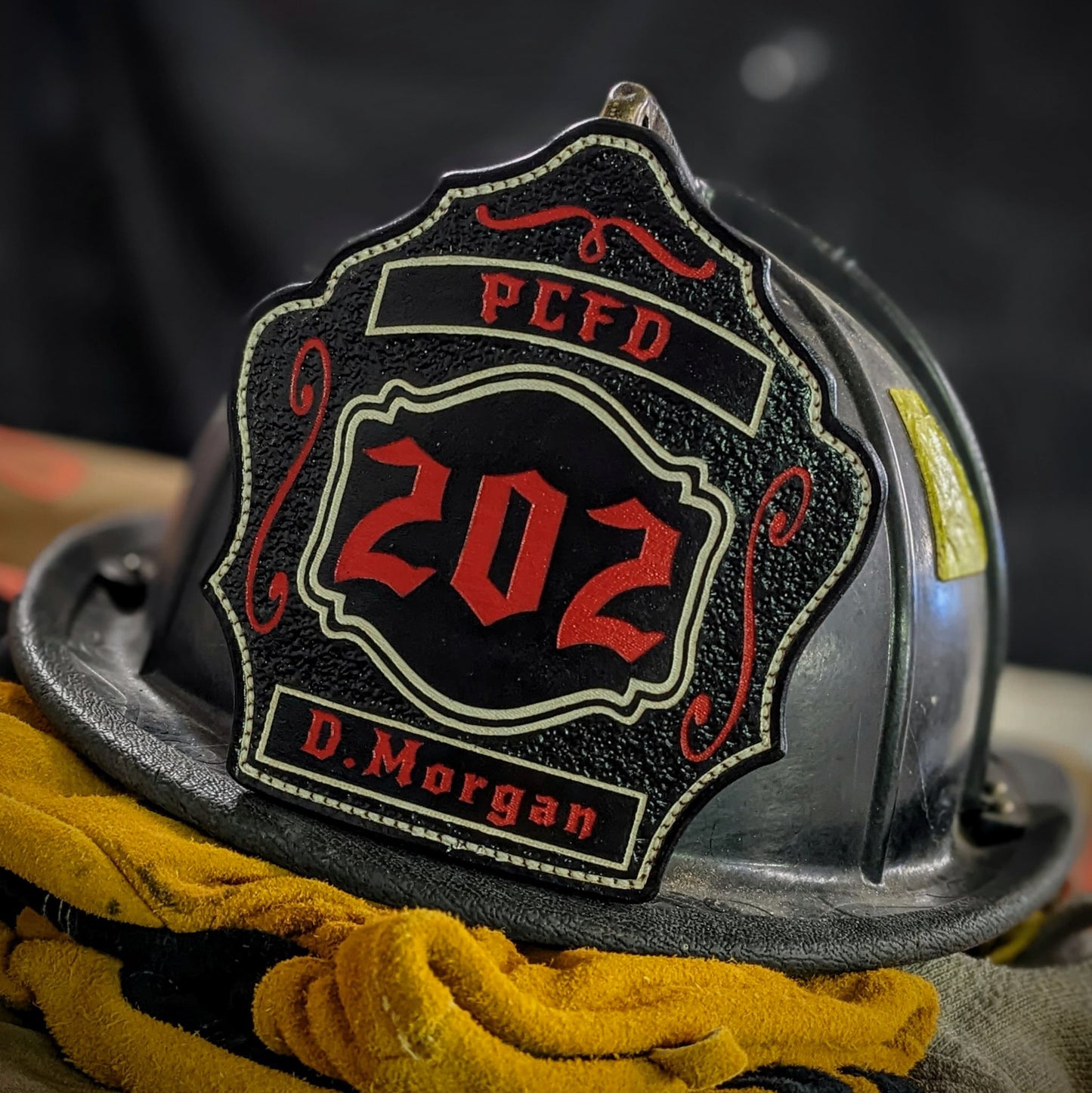 Custom black leather firefighter helmet shield with number 202 in red, red banners, and scroll accents