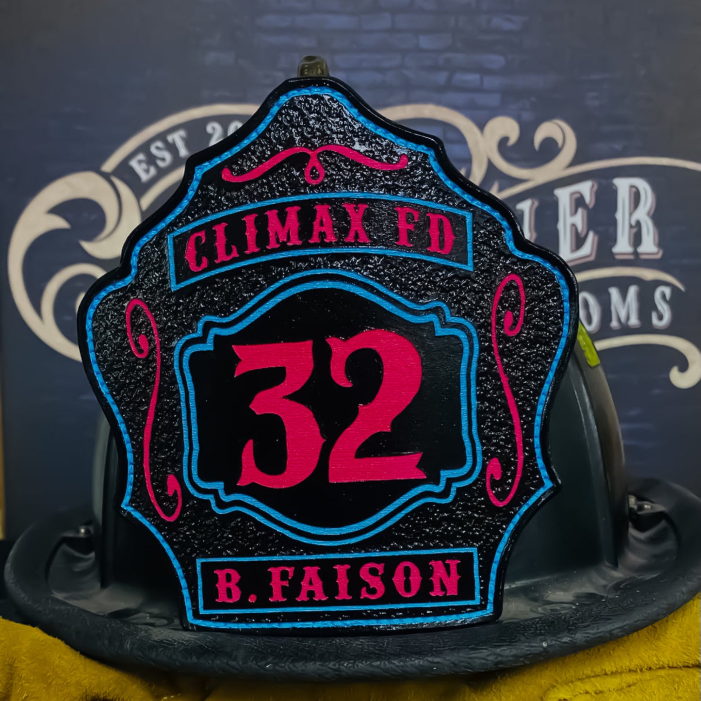 Black leather firefighter helmet shield with bright pink number 32, top banner Climax FD, bottom banner B. Faison, accented with neon blue and pink detailing.