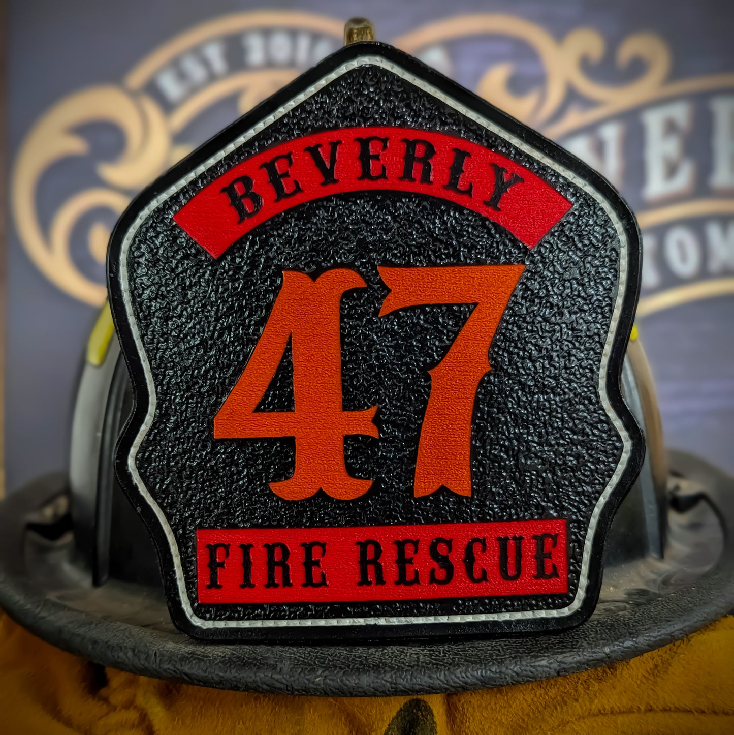 Black leather firefighter helmet shield with bold orange number 47, red panels reading Beverly and Fire Rescue, white border trim, mounted on a fire helmet.