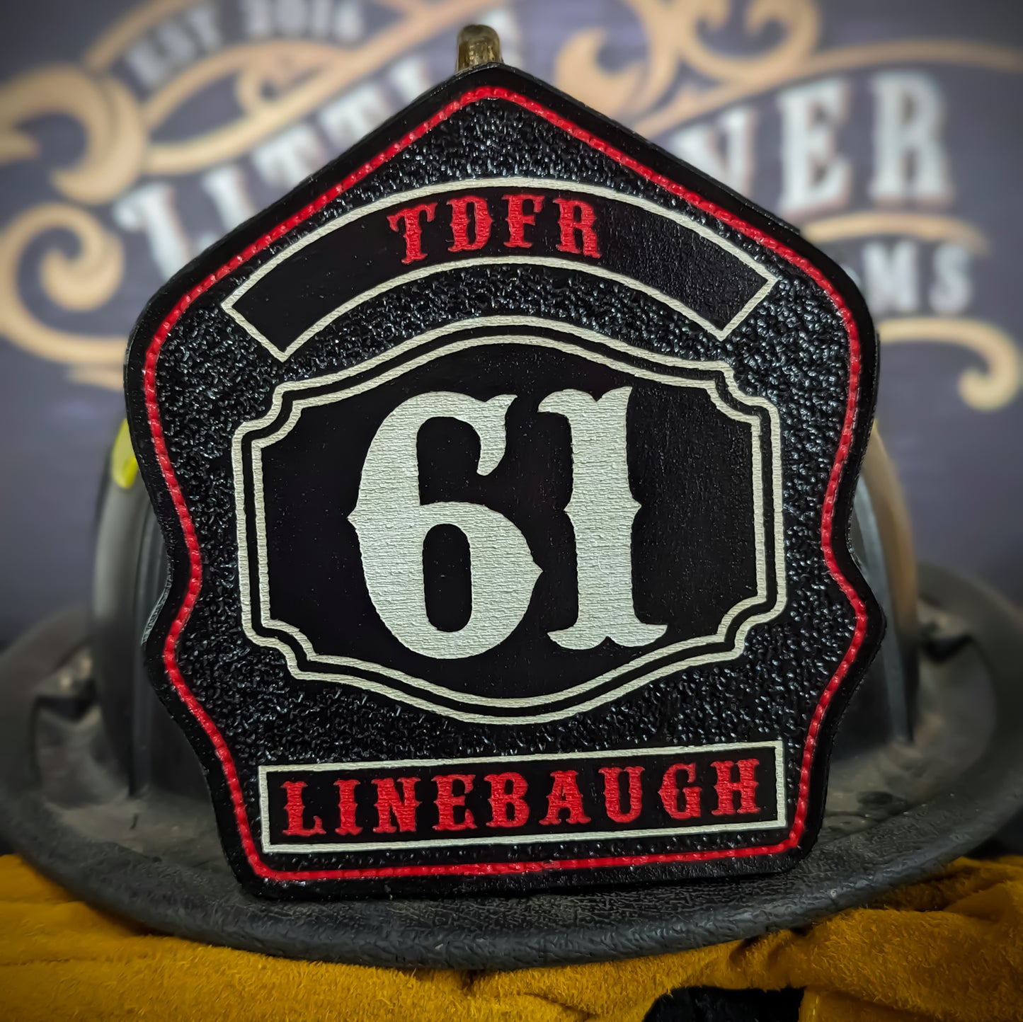 Black leather firefighter helmet shield with bold white number 61, red text panels reading TDFR and Linebaugh, detailed white border, mounted on a fire helmet.