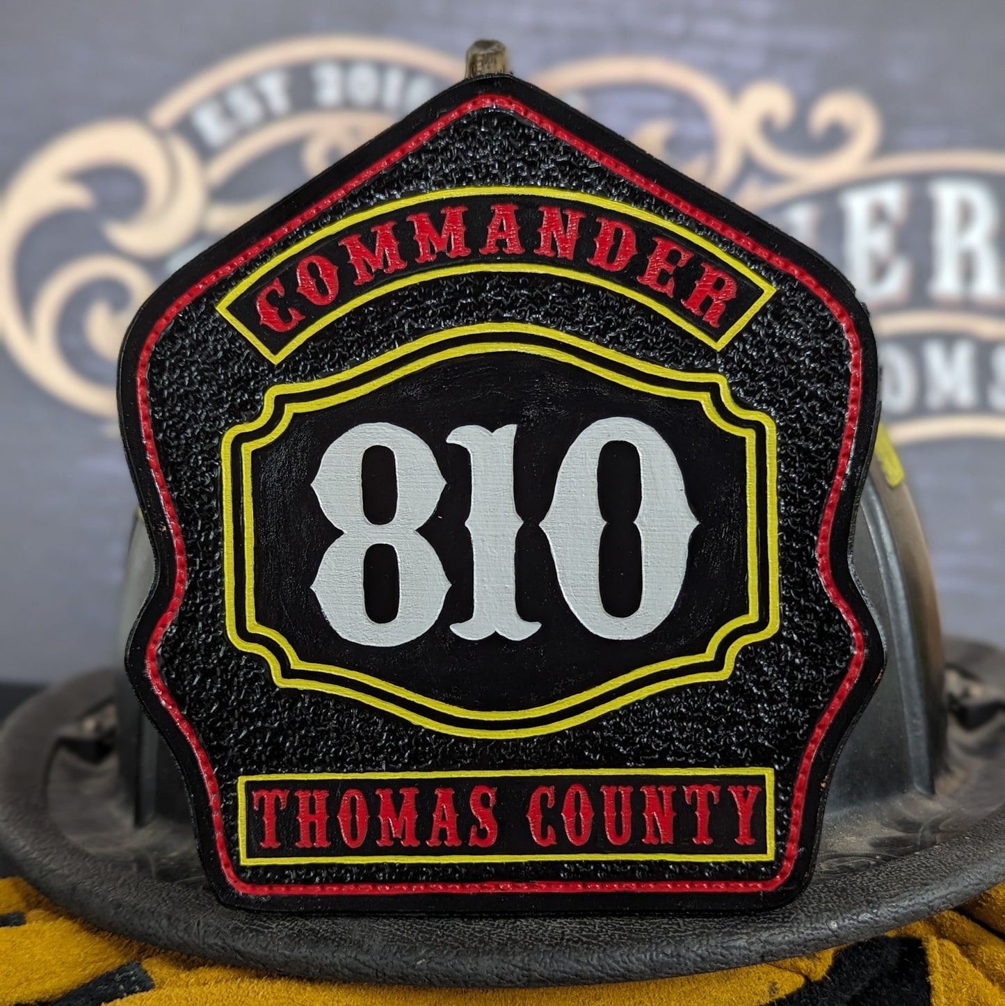 Black leather firefighter helmet shield with bold white number 810, yellow border, red Commander title at top, and Thomas County at bottom.