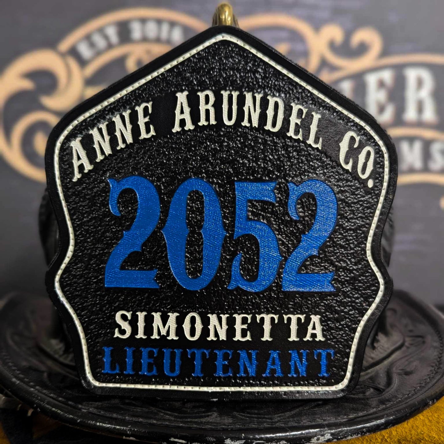 Custom leather firefighter helmet shield featuring Anne Arundel County design with lieutenant rank and bold blue numbering.