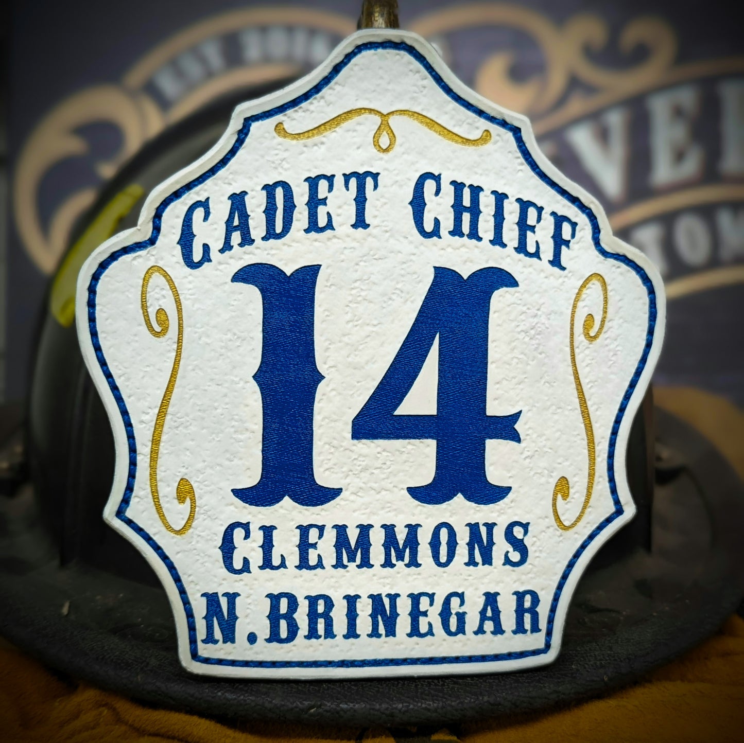 White leather firefighter helmet shield with Cadet Chief lettering, bold blue number 14, and Clemmons N. Brinegar details.