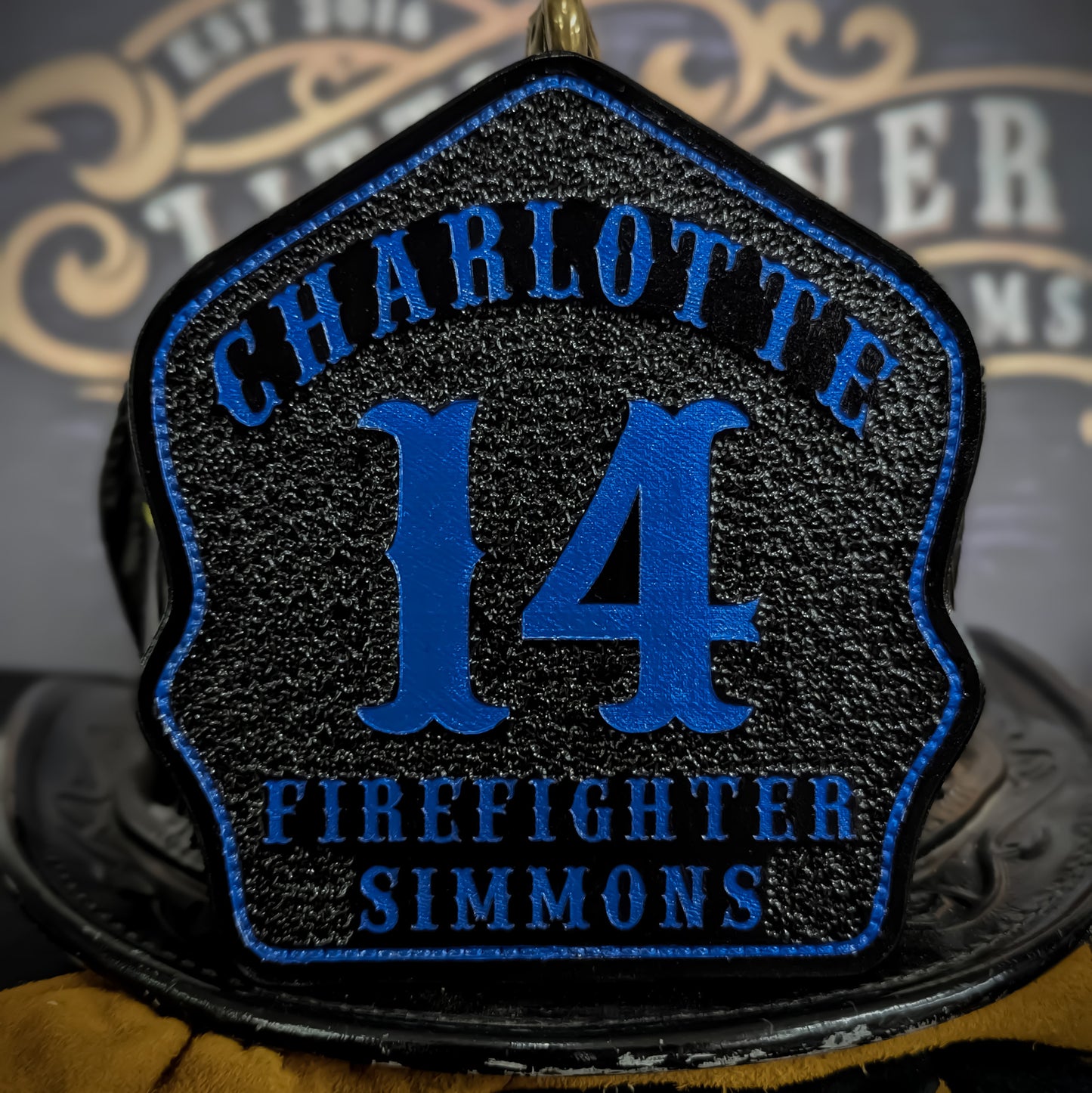Custom black leather firefighter helmet shield with Charlotte lettering, bold blue number 14, and firefighter name.