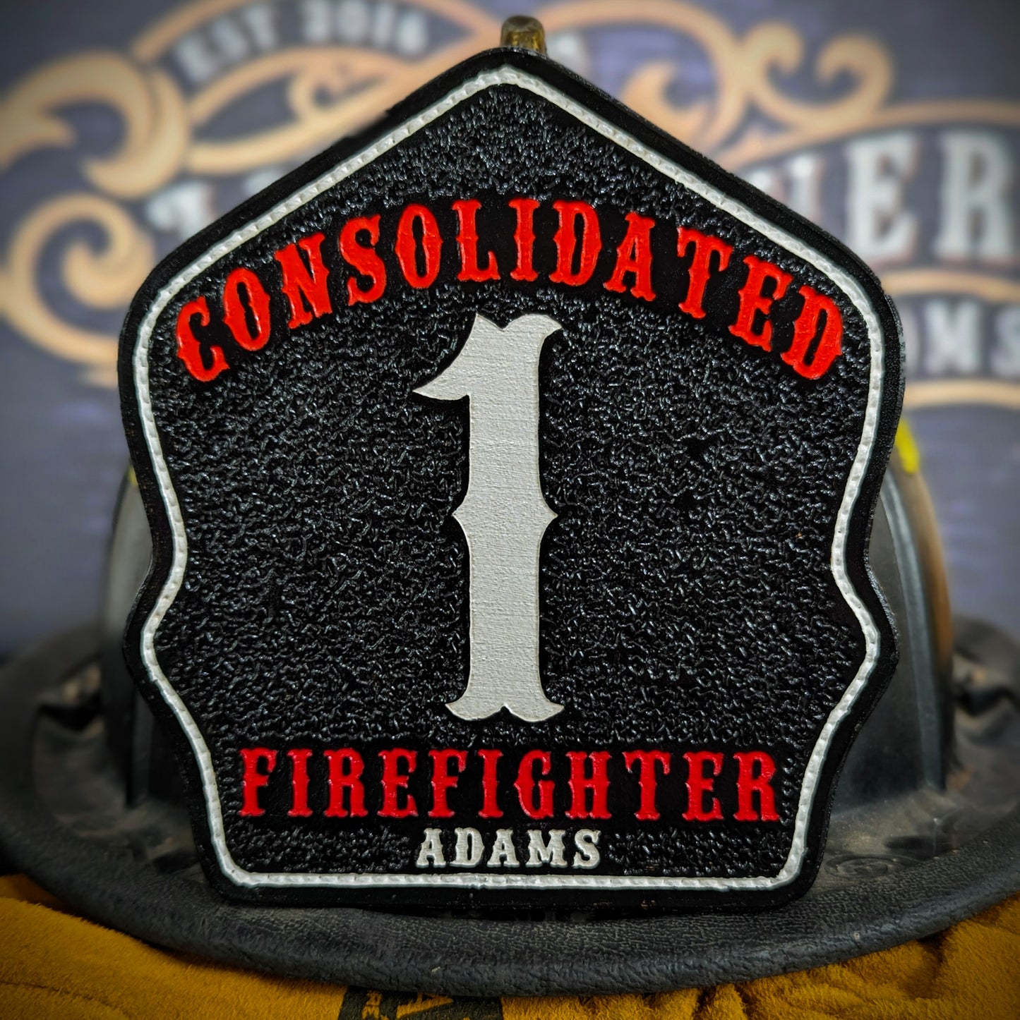 Custom black leather firefighter helmet shield with Consolidated lettering, bold white number 1, and firefighter Adams name.