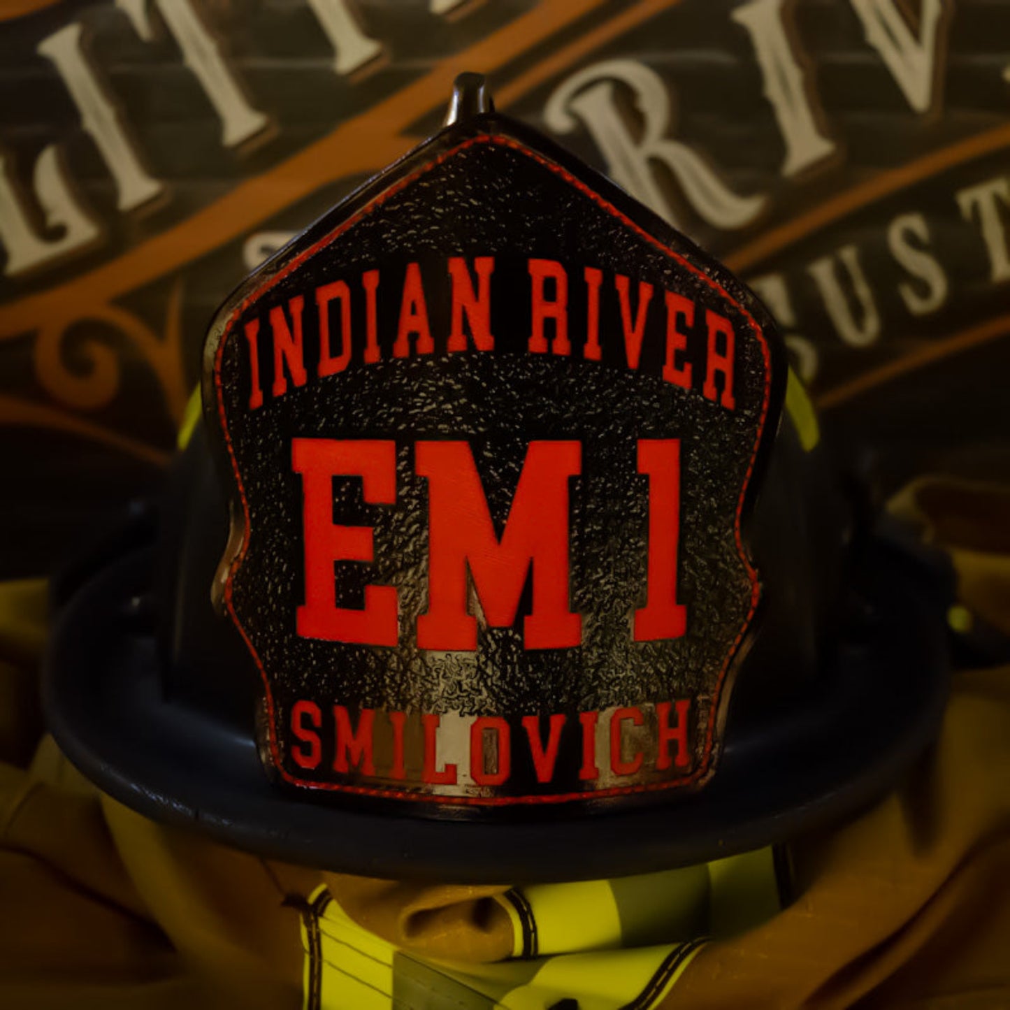 Custom firefighter helmet shield in black leather with Indian River design and bold red EM1 lettering.
