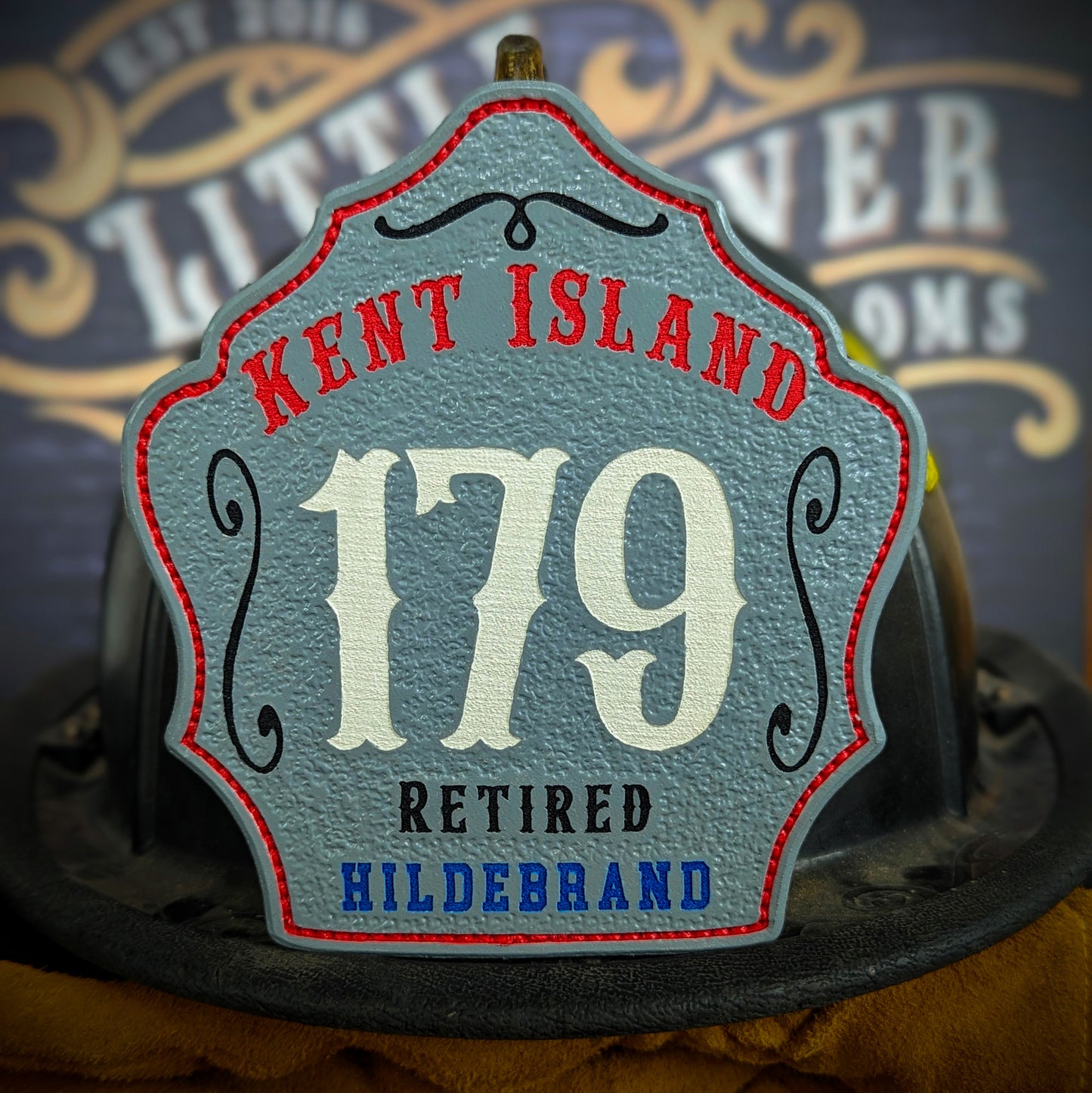 Gray leather firefighter helmet shield with Kent Island lettering, white number 179, and retired Hildebrand details.