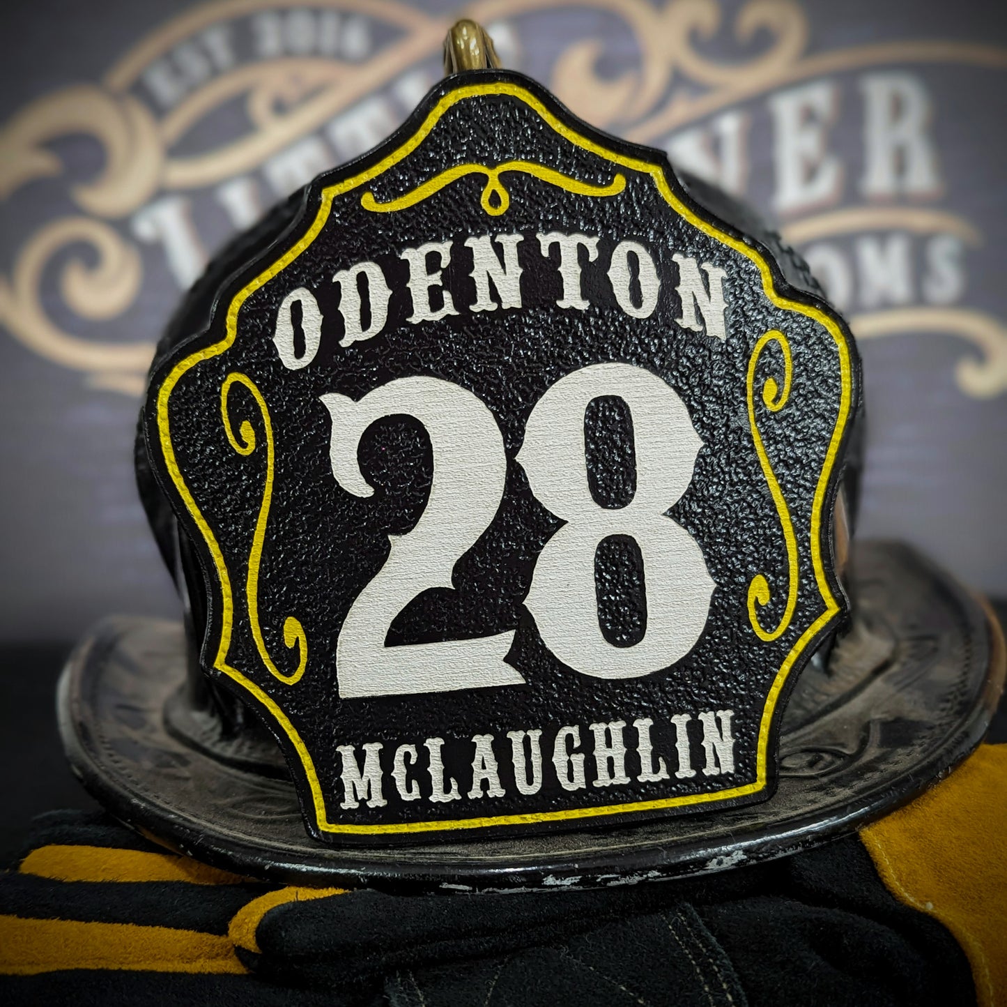 Black leather firefighter helmet shield with Odenton lettering, bold white number 28, and McLaughlin name.