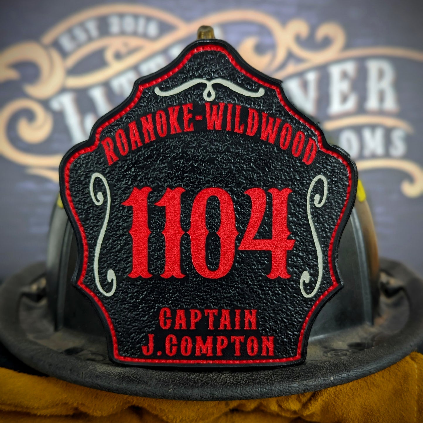 Black leather firefighter helmet shield with Roanoke Wildwood lettering, red number 1104, and captain J. Compton details.