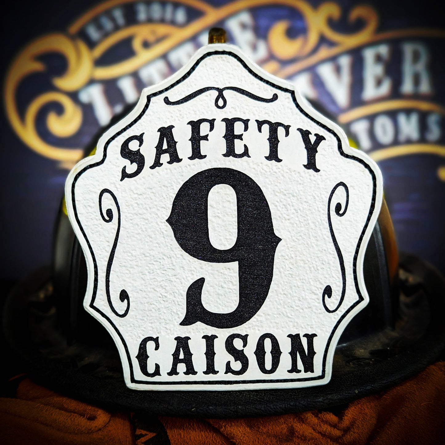 White leather firefighter helmet shield with Safety title, large black number 9, and Caison name.