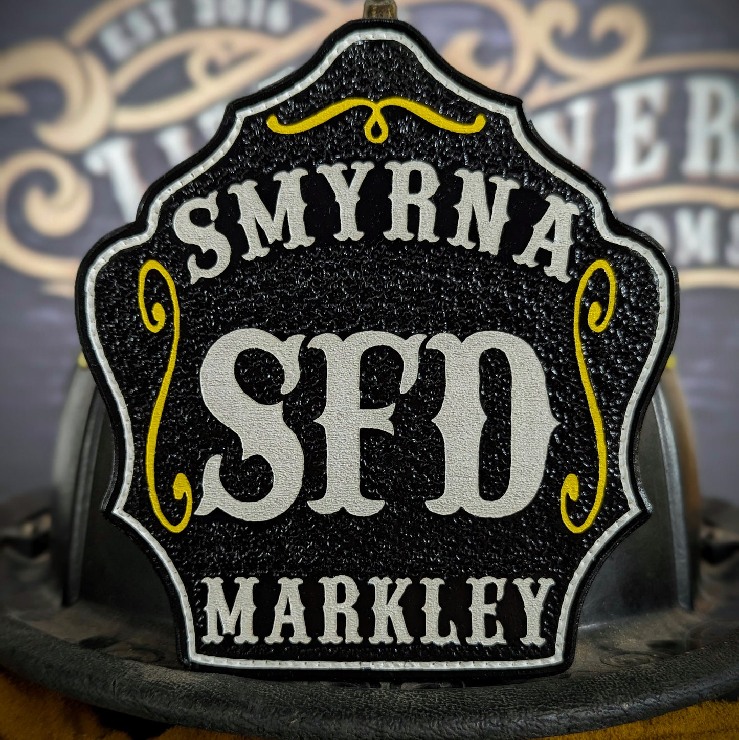 Black leather firefighter helmet shield with Smyrna SFD design, bold white letters, and Markley name.