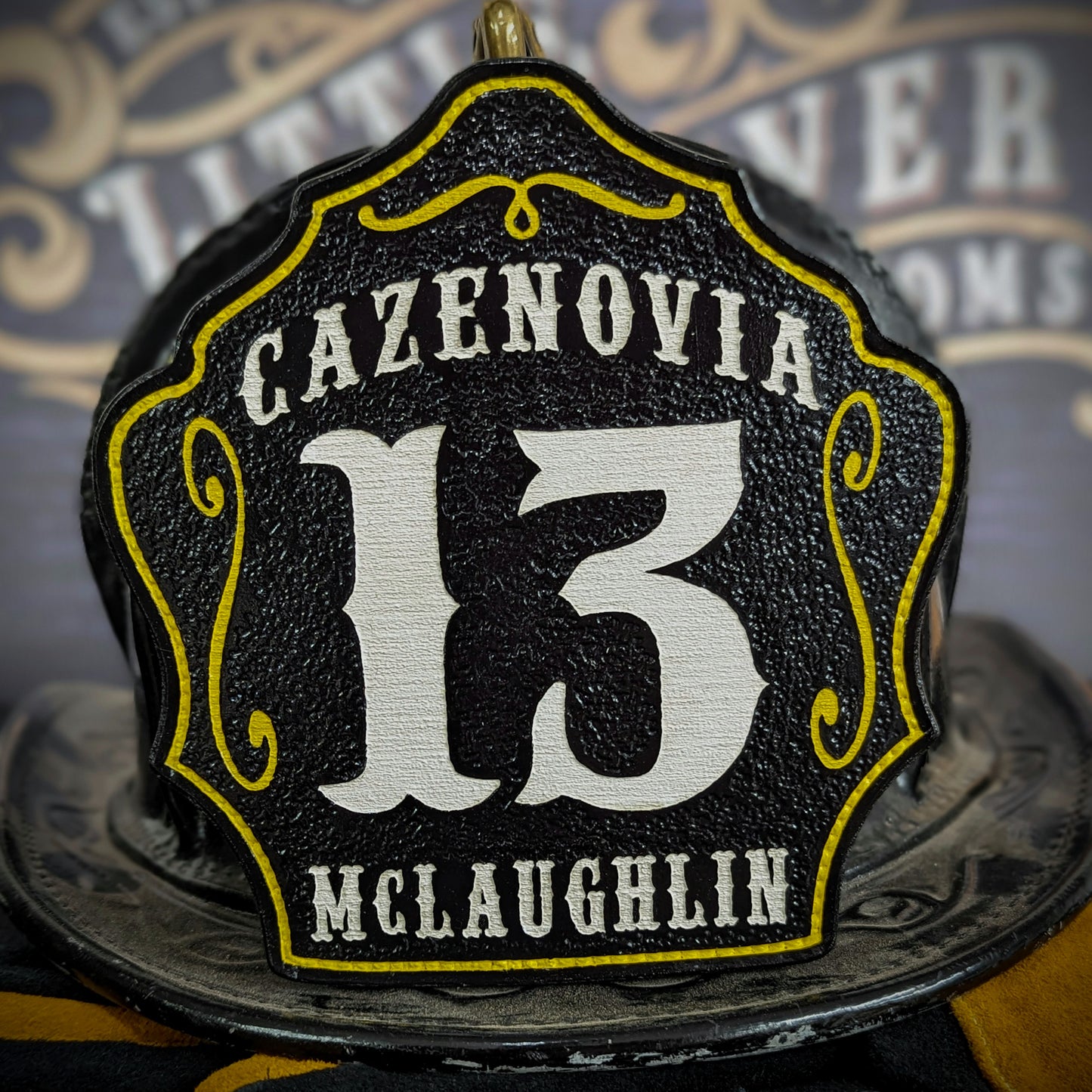Custom leather firefighter helmet shield for Cazenovia, black with white 13 and McLaughlin name, yellow outline and scrolls, Little River Customs