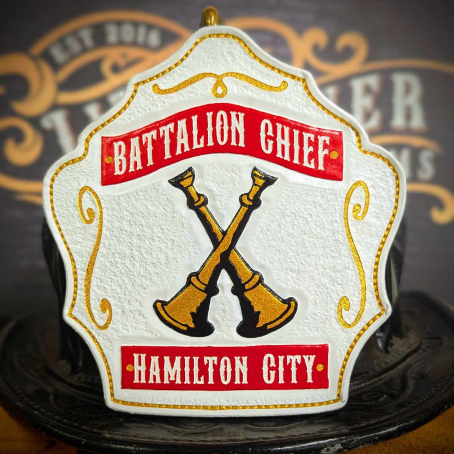 White firefighter helmet shield with red banners and gold crossed bugles on a black outline.