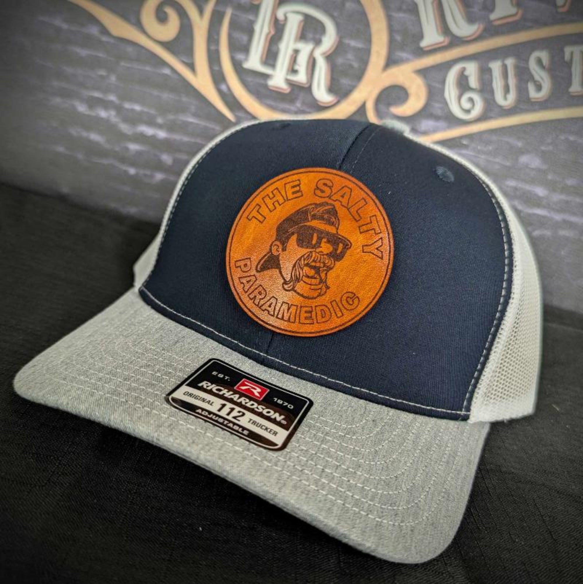 Custom firefighter and EMS hats featuring The Salty Paramedic's leather patch design, shown on Richardson 112 and 110 hats for first responders.