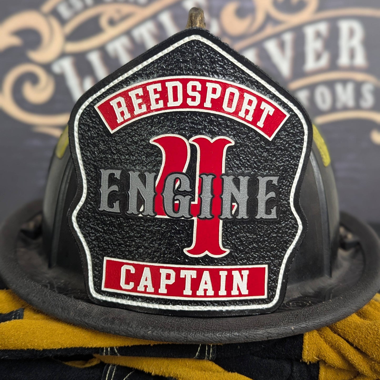 Custom leather firefighter helmet shield on a textured black field with classic engine layout—hand-painted, helmet mounted.