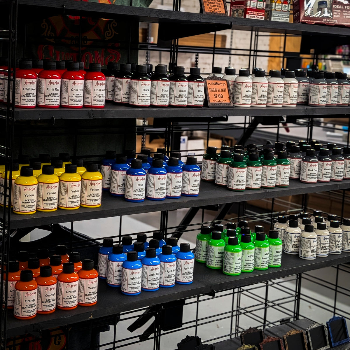 Assorted colors of Angelus acrylic leather paint in 4 oz bottles on shop shelves.