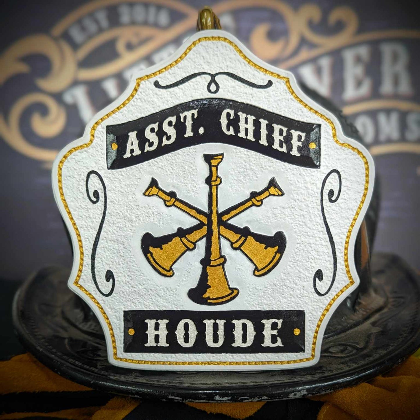 Assistant chief helmet shield in warm tan with gold crossed bugles and red accents.