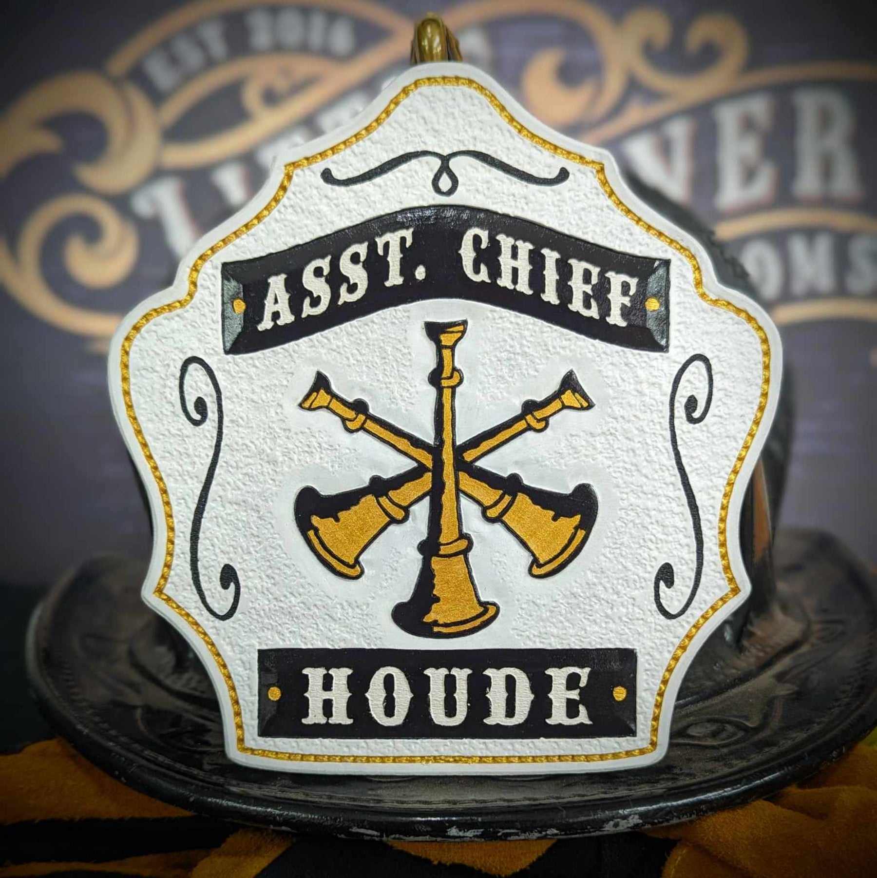 Assistant chief helmet shield in warm tan with gold crossed bugles and red accents.