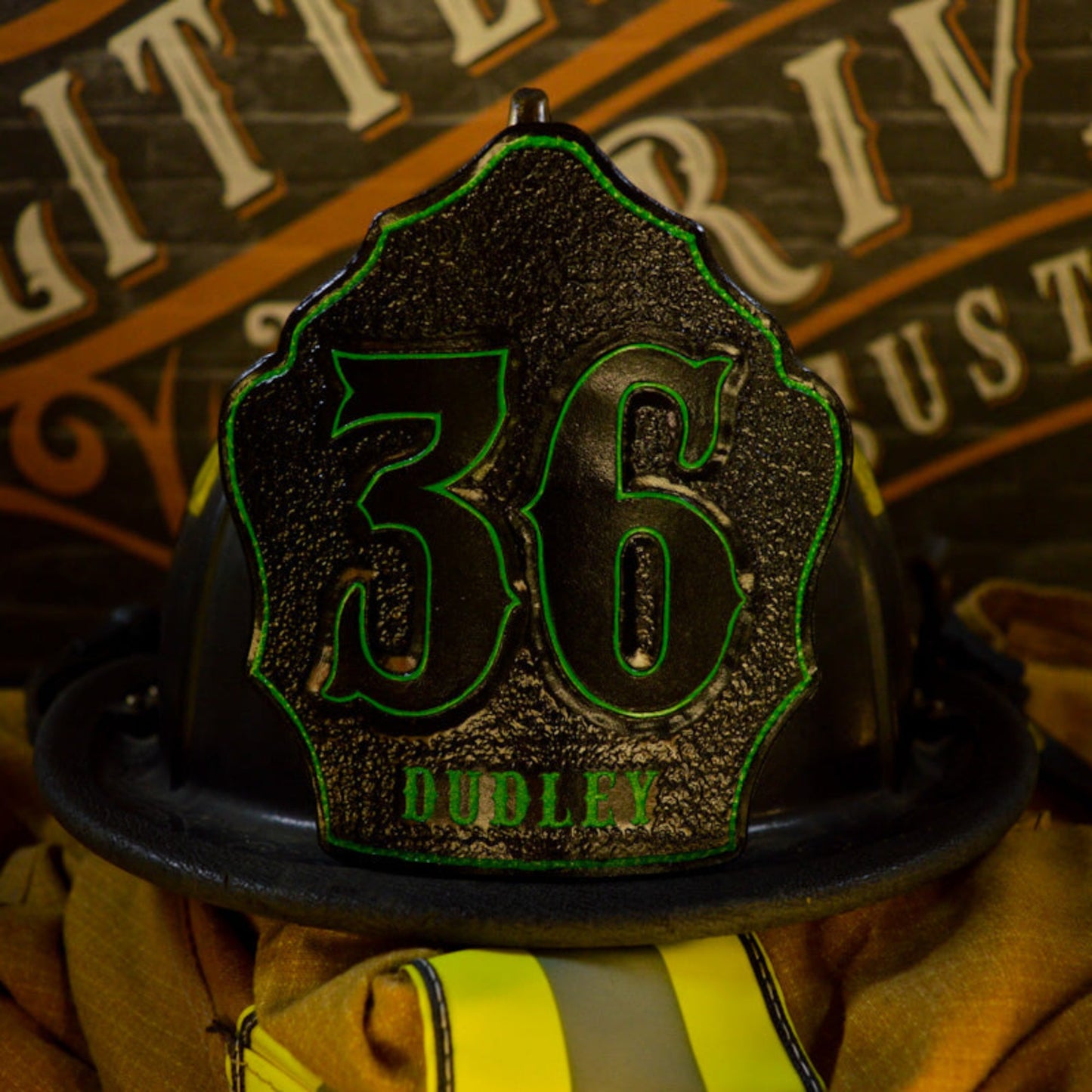 Black leather firefighter helmet shield with large “36” and neon-green outline, “DUDLEY” name at the base—mounted on a helmet.
