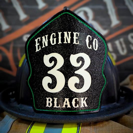 Black leather firefighter helmet shield with “ENGINE CO” at the top, large white numerals “33,” green edge outline, and “BLACK” name—mounted on a helmet.