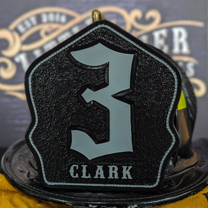 Black leather firefighter helmet shield with large gray gothic numeral “3” and gray name lettering “CLARK”—mounted on a helmet.