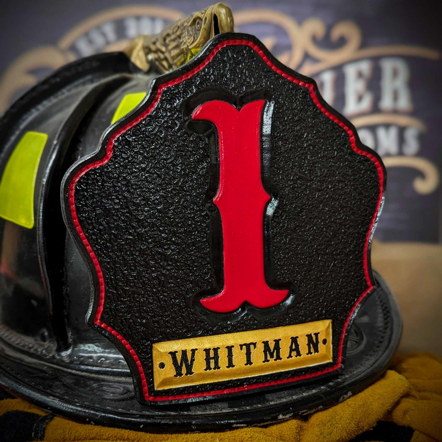 Black leather firefighter helmet shield with tall red numeral “1” and a gold nameplate reading WHITMAN—mounted on a helmet.