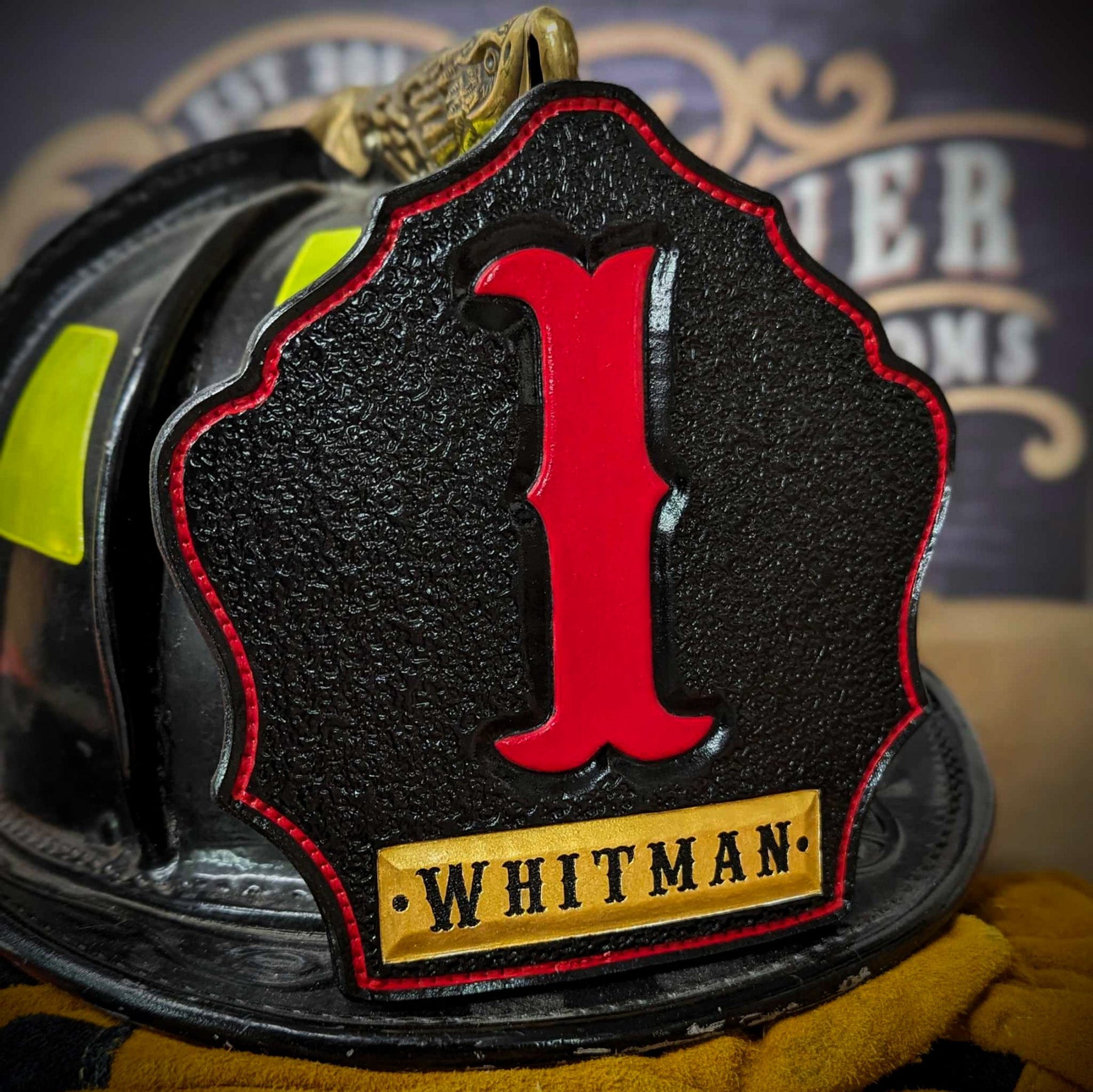 Black leather firefighter helmet shield with tall red numeral “1” and a gold nameplate reading WHITMAN—mounted on a helmet.
