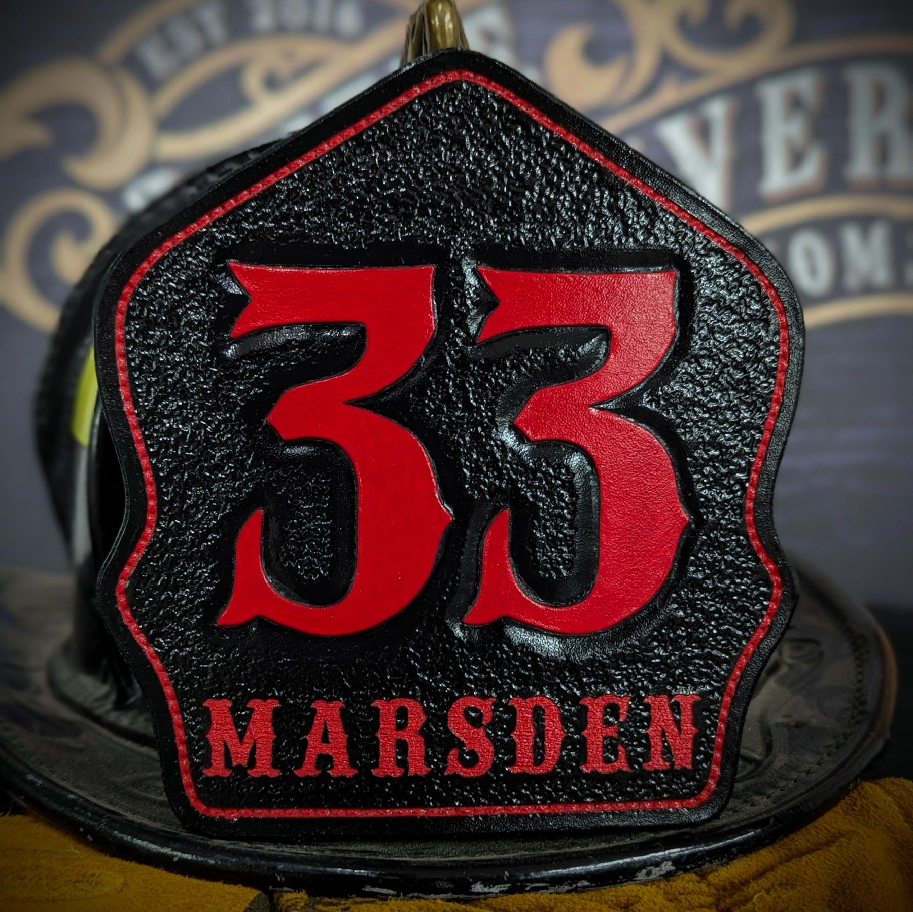 Black leather firefighter helmet shield with oversized red numerals “33,” red border outline, and “MARSDEN” name lettering—mounted on a helmet.