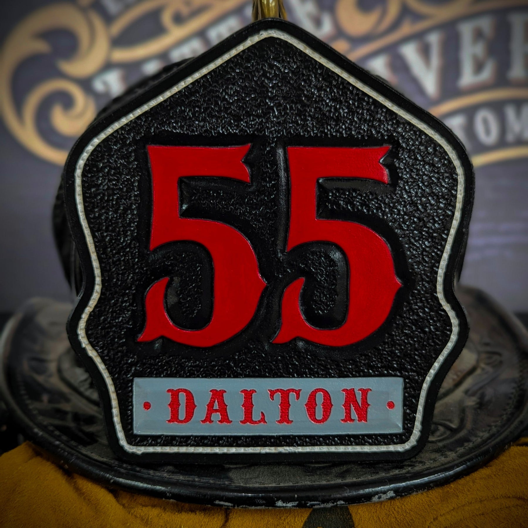 Black leather firefighter helmet shield with large red numerals “55” and a gray nameplate reading DALTON—mounted on a helmet.