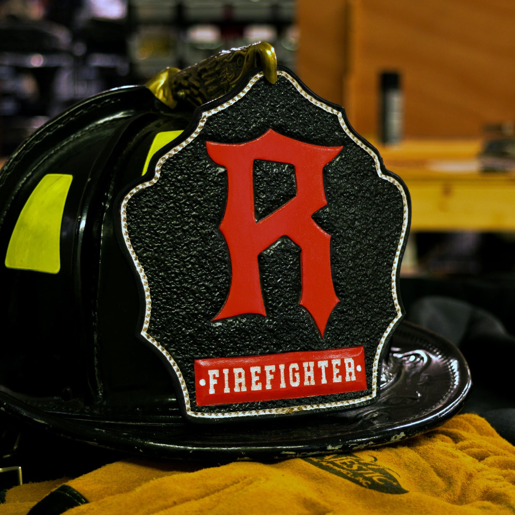 Black leather firefighter helmet shield with large red initial “R” and a red “FIREFIGHTER” banner, white trim—mounted on a helmet.