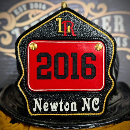 Black leather firefighter helmet shield with red inset number plate, gold rivets, LR monogram, and “Newton NC” title—mounted on a helmet.