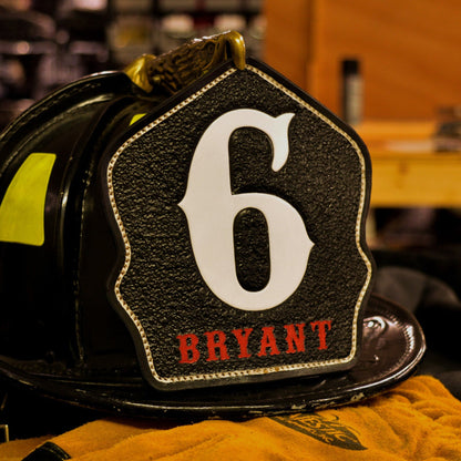 Black leather firefighter helmet shield with large white numeral “6” and red name lettering “BRYANT”—mounted on a helmet.