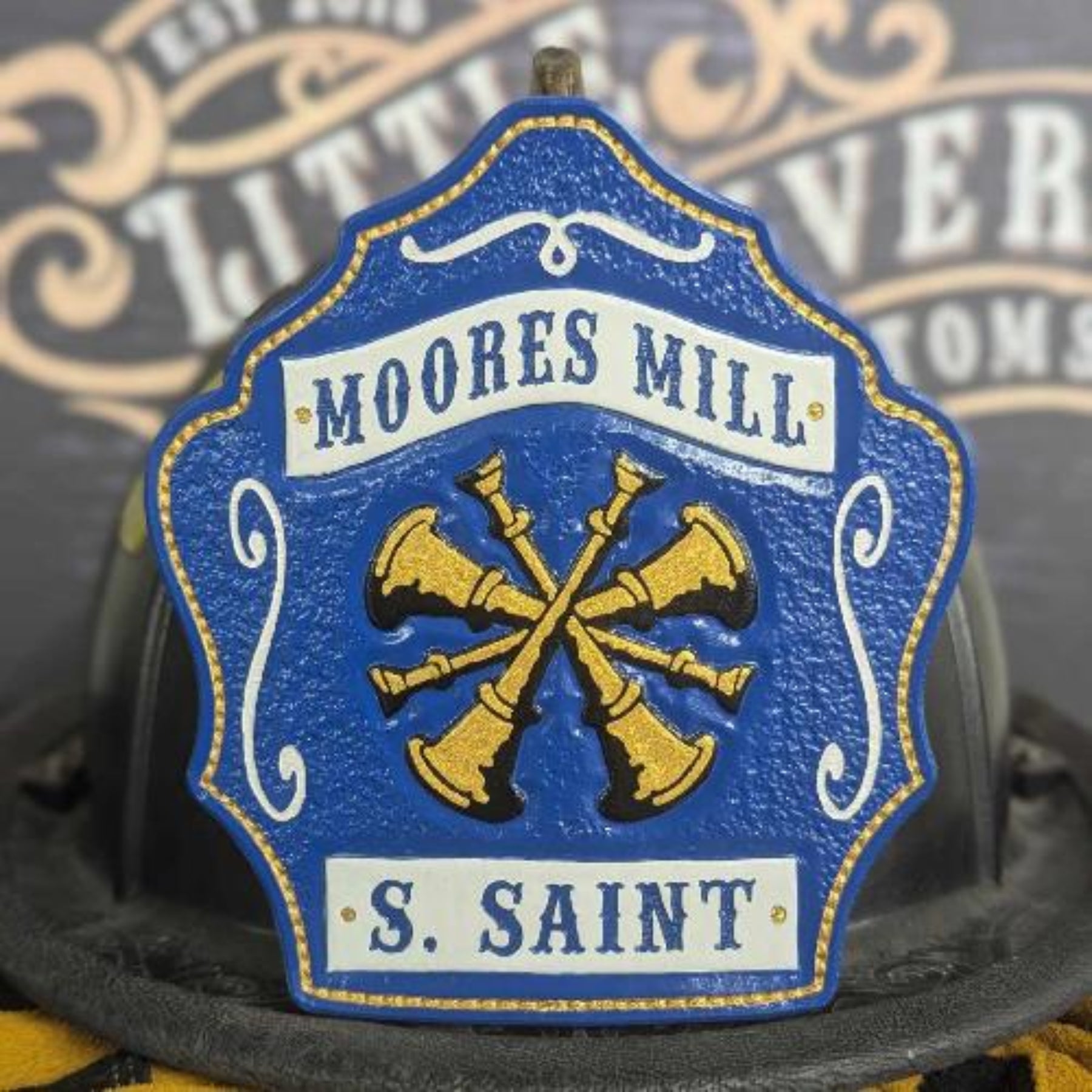 Blue leather firefighter helmet shield with gold crossed bugles and white banners—hand-painted, helmet mounted.