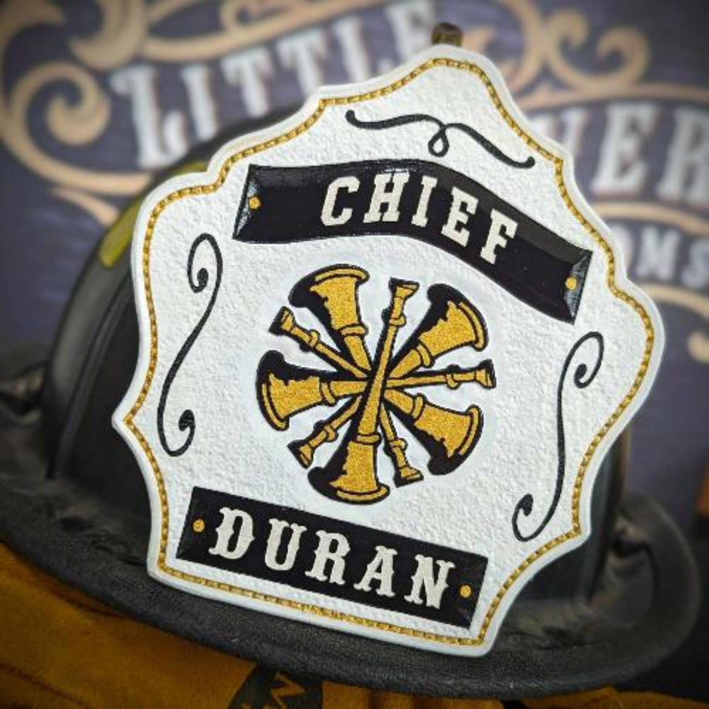 Chief-style white helmet shield with gold crossed bugles and bold black outline.