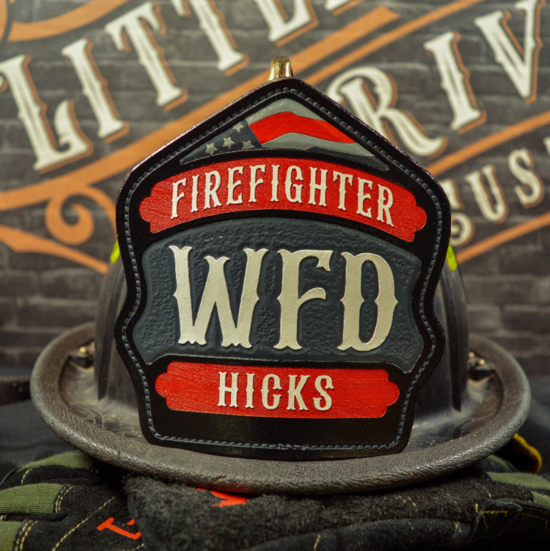 Custom leather firefighter helmet shield with red top and bottom banners, gray center panel, and subtle flag detail—hand-painted and mounted on a helmet.