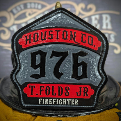 Custom leather firefighter helmet shield with textured gray center panel, red top and bottom banners, and raised black numerals—hand-painted and mounted on a helmet.