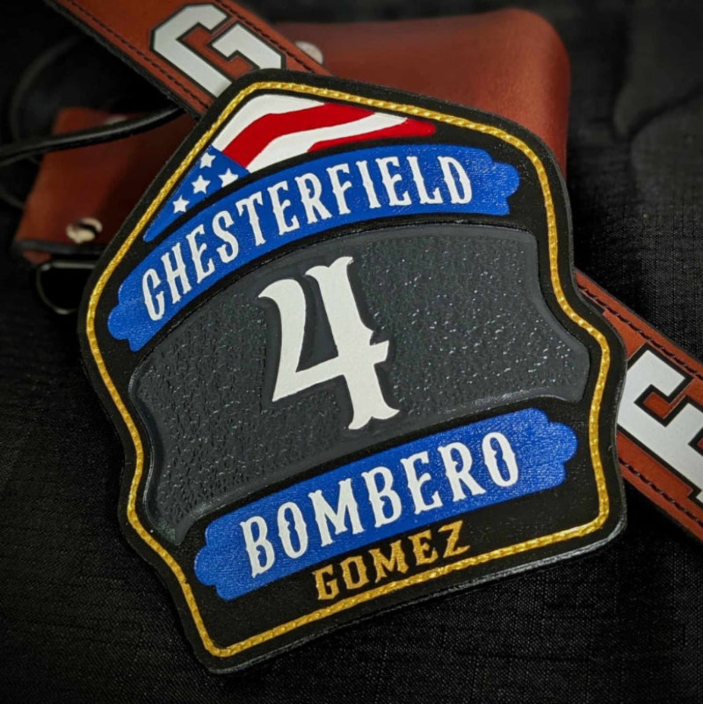 Custom leather firefighter helmet shield with gray center panel, blue lower banner, red arch, and gold trim—hand-painted.