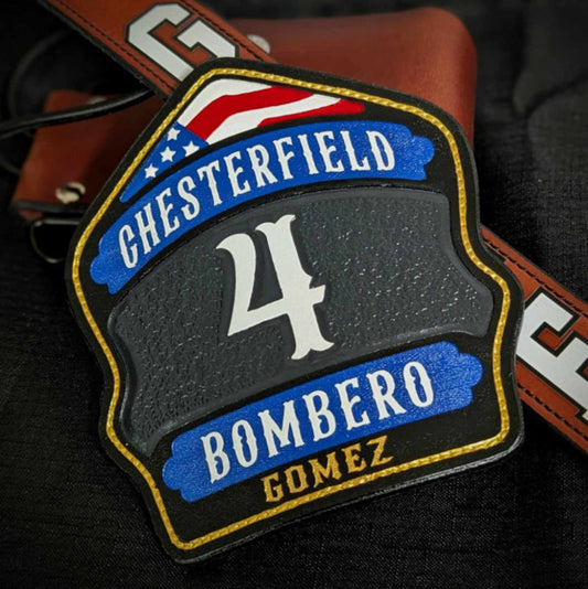 Custom leather firefighter helmet shield with gray center panel, blue lower banner, red arch, and gold trim—hand-painted.