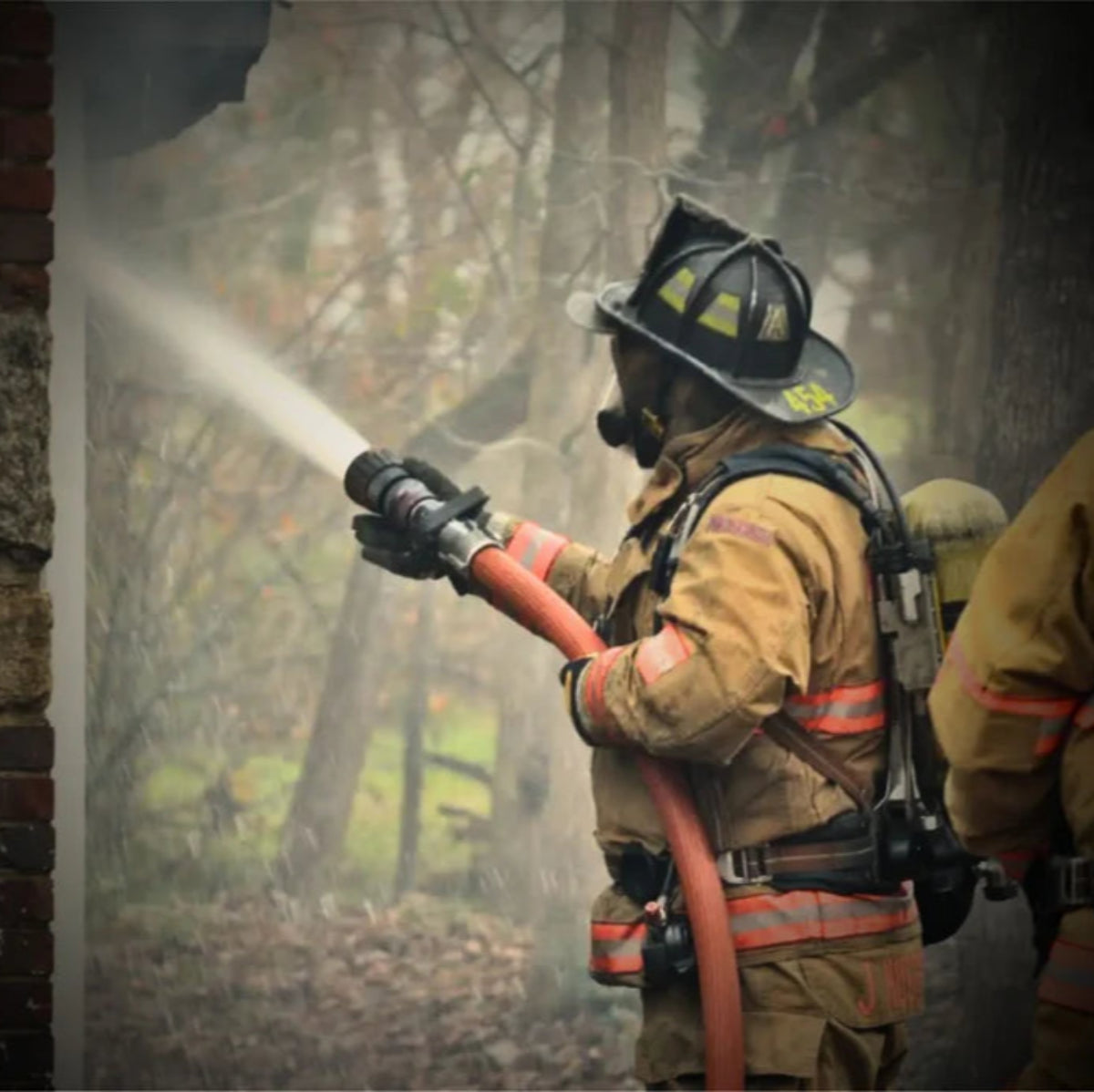 Firefighter in full gear spraying water during fireground operations with helmet and hose