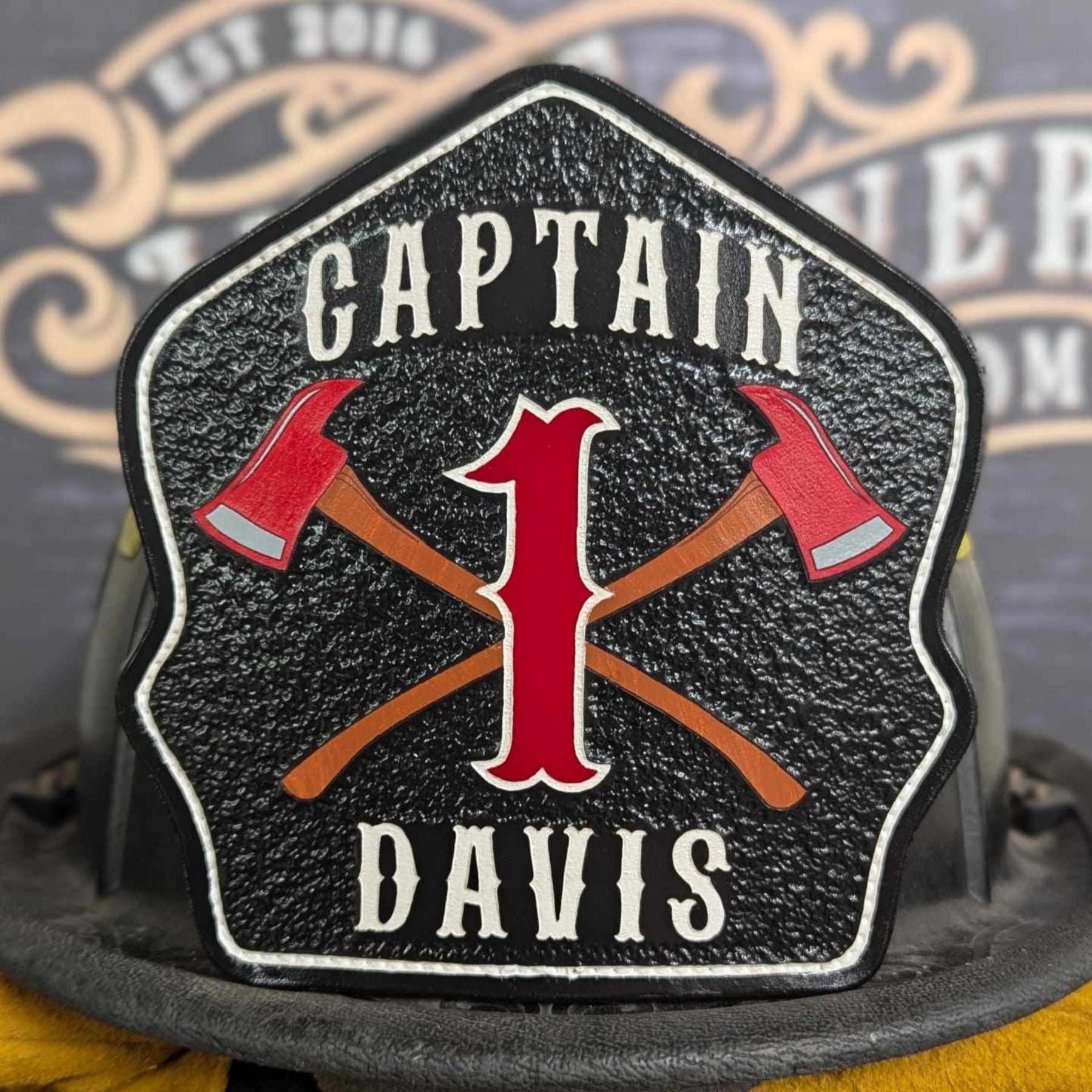 Black leather firefighter helmet shield with crossed red axes and bold red number 1, custom fire department gear.