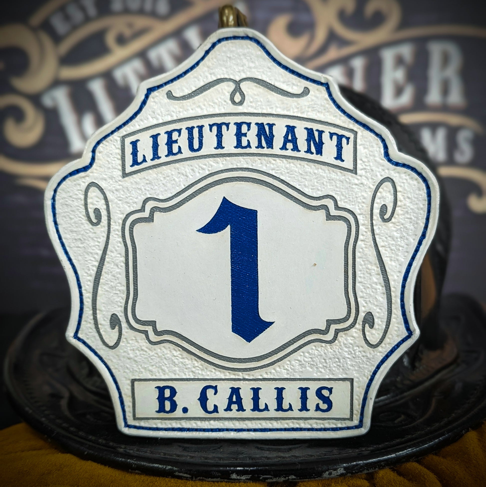 White leather firefighter helmet shield with bold blue number 1, Lieutenant title at top, and name B. Callis at bottom with blue accents.