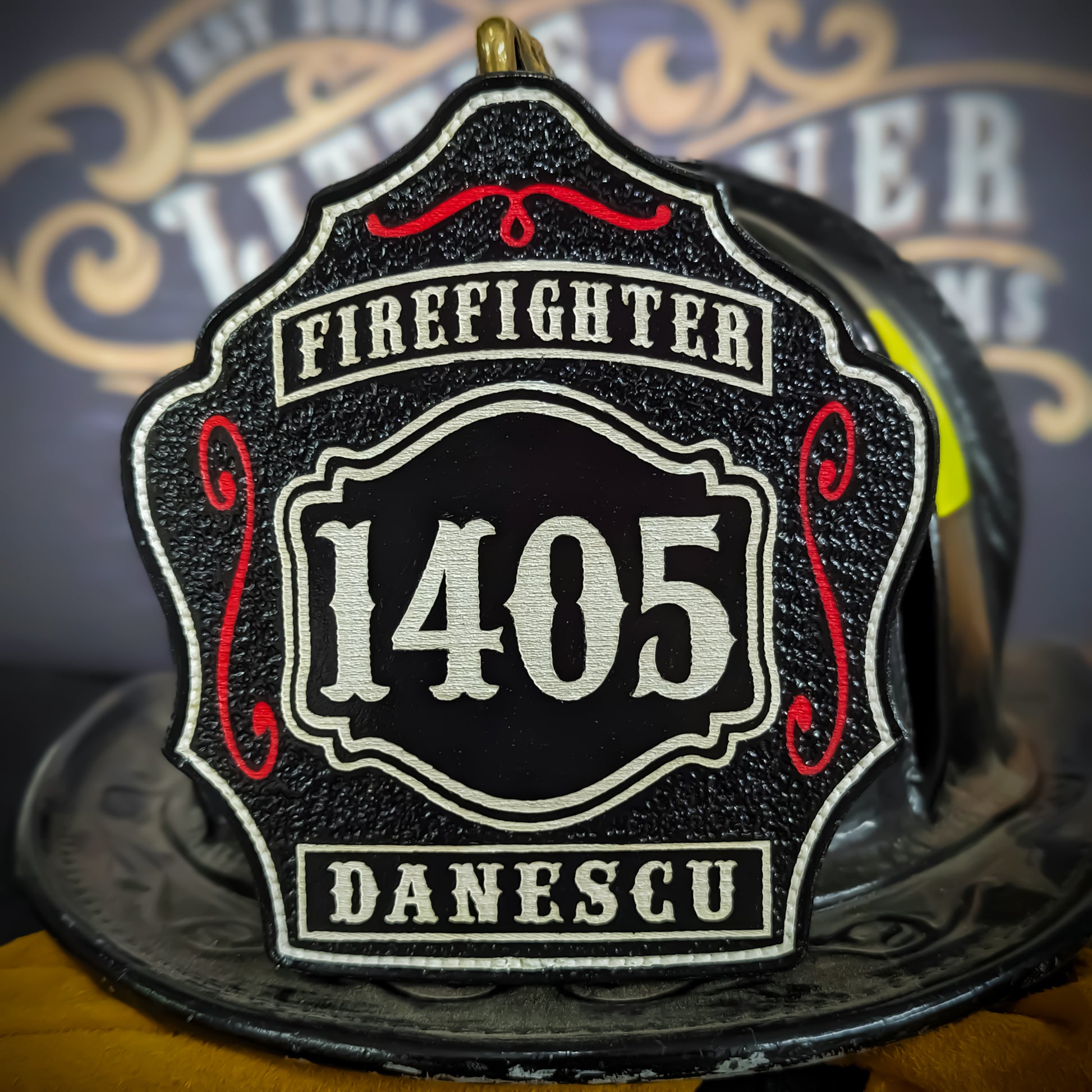 Black leather firefighter helmet shield with bold white number 1405, white text panels reading Firefighter and Danescu, red scroll accents, mounted on a fire helmet.