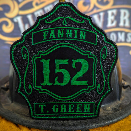 Black leather firefighter helmet shield with bright green number 152, green text panels reading Fannin and T. Green, decorative scroll accents, mounted on a fire helmet.